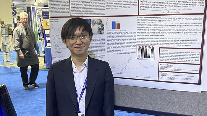 Joe Truong stands in front of his poster pressentation at a research conference.