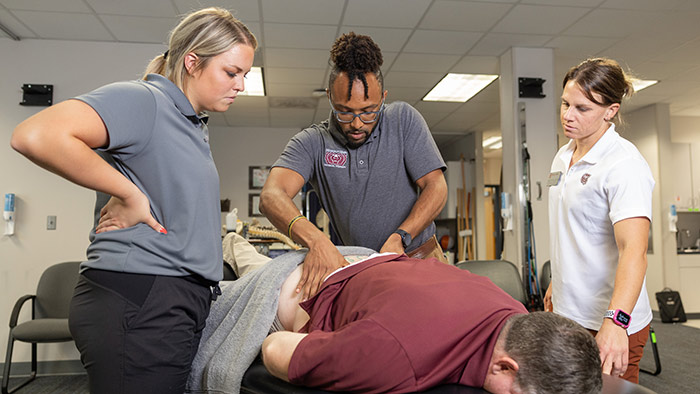 William Smith practices spine care techniques on a patient at the Missouri State physical therapy clinic. A classmate and professor are beside him, watching closely.