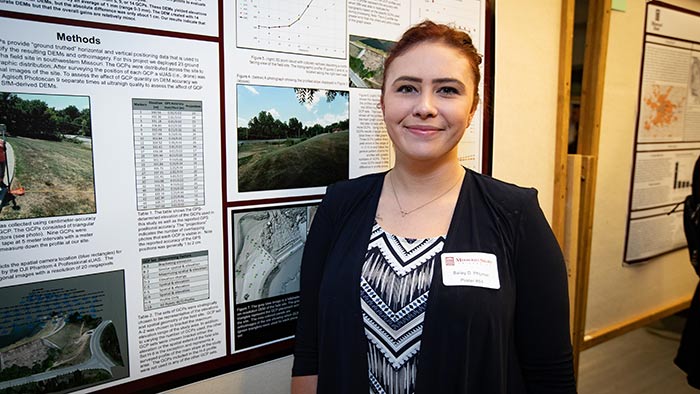 Bailey Wolf posing next to presentation poster at CNAS Undergraduate Research Day.