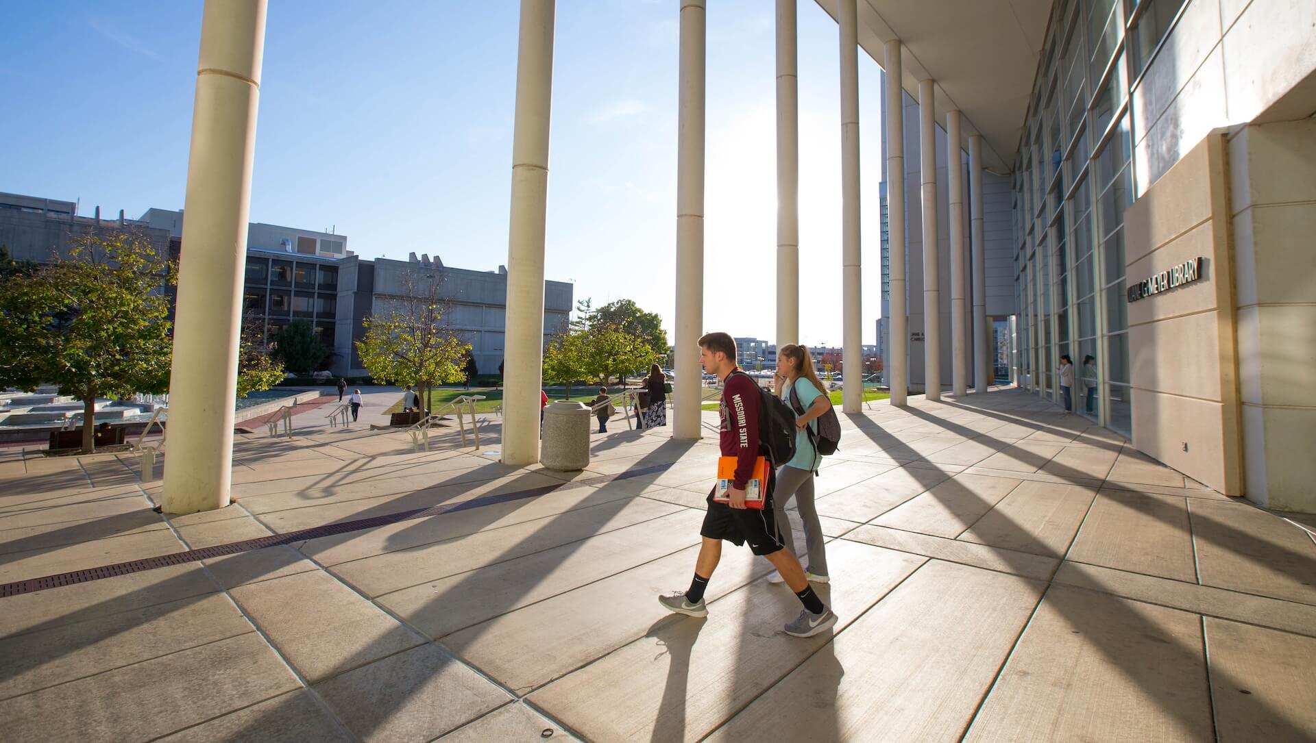 The Meyer Library columns cast long, elegant shadows across the ground as two students exit the library.
