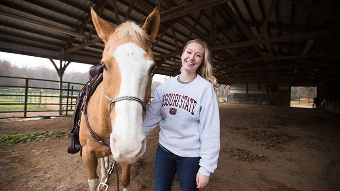 Emily Hrpcha with horse in stable.