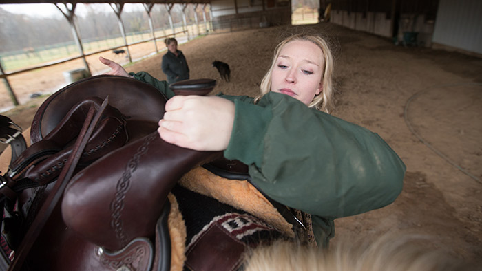 Emily Hrpcha attending to horse in stable.