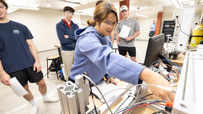 Ana Torres setting up an experiment during an engineering lab. Classmates are watching her prepare a machine for use.